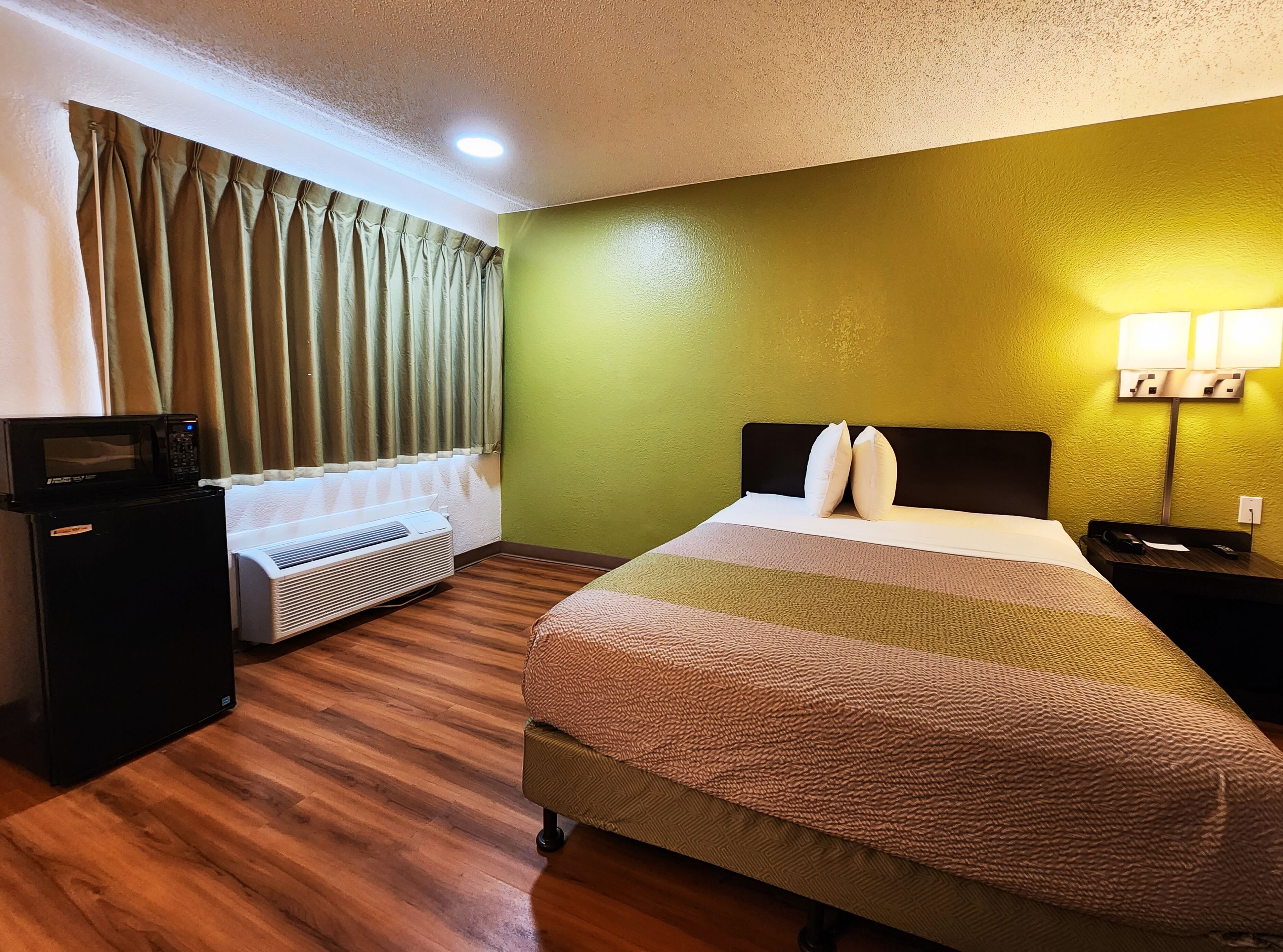 A hotel room with a bed, a flat-screen TV, a heater, and a lamp.