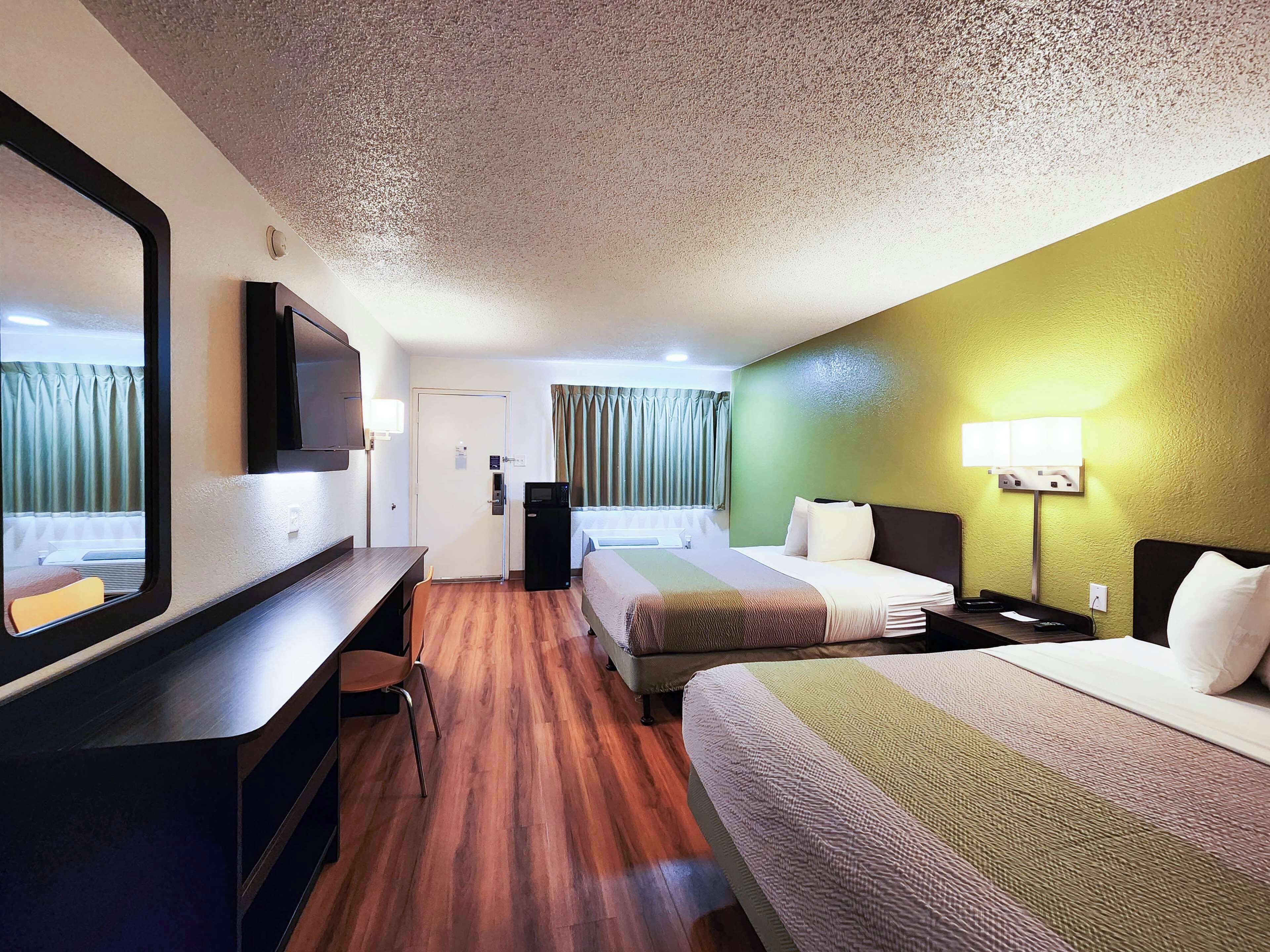 A hotel room with two beds, a desk, a TV, and a door.