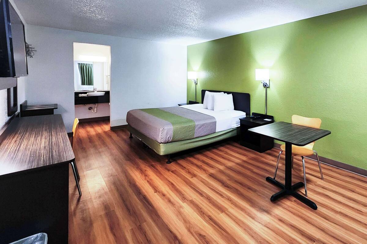 A hotel room with a bed, bedside table, desk, chair, and a small table with a chair.