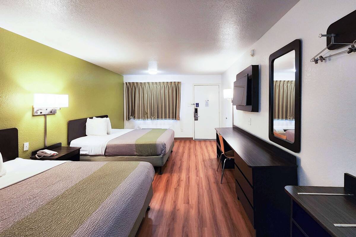 A hotel room with two beds, a desk, a chair, a television, and a mirror.