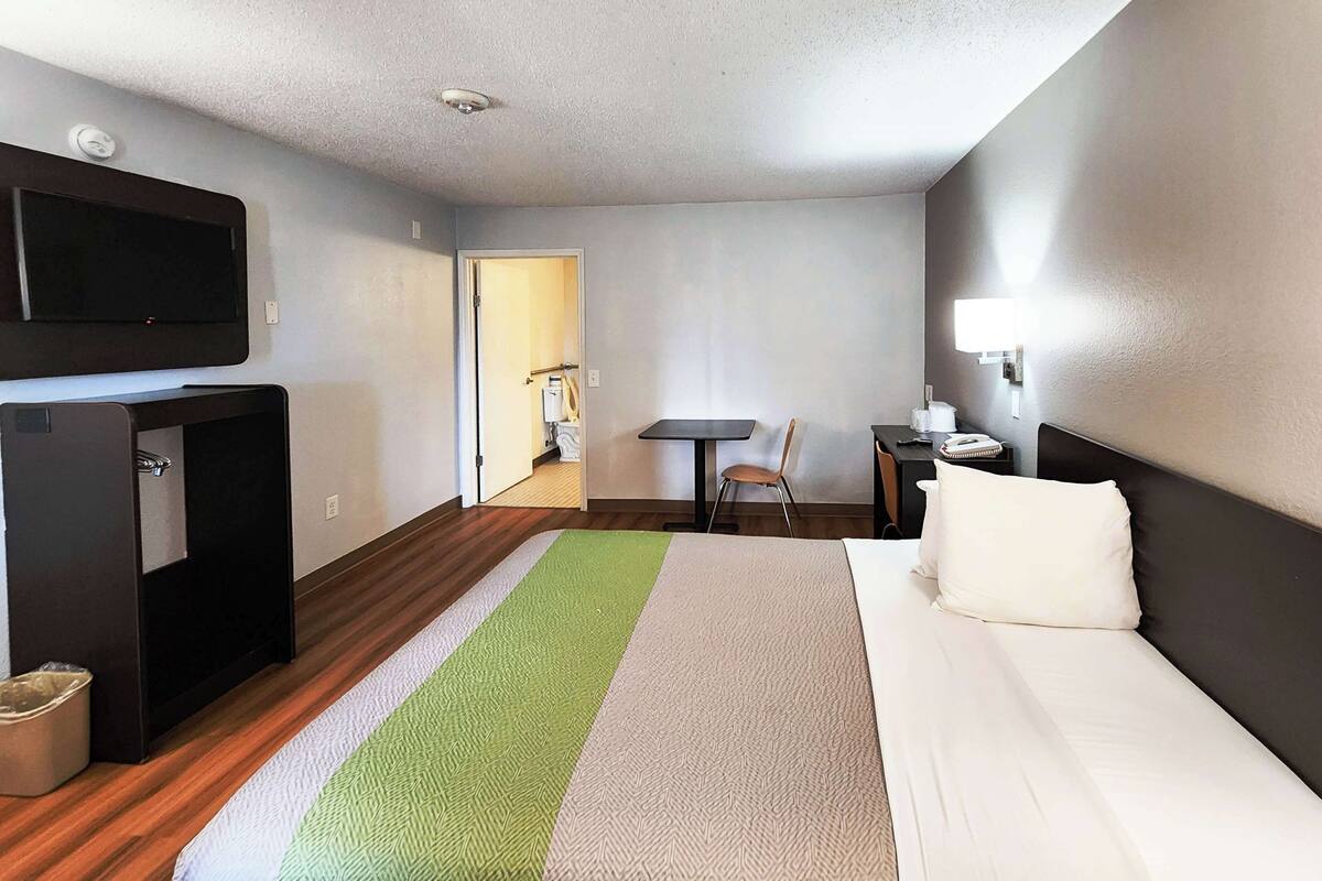 A hotel room with a bed, a desk, a chair, a television, and a small table.