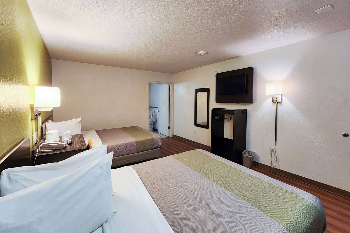 A hotel room with two beds, a desk with a telephone and glasses, a mirror, a television, and a trash bin.
