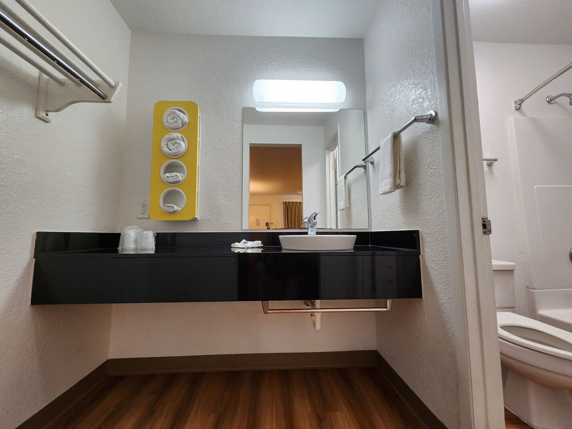 Un baño con tocador negro, lavamanos blanco, espejo y toallero amarillo con cuatro toallas.