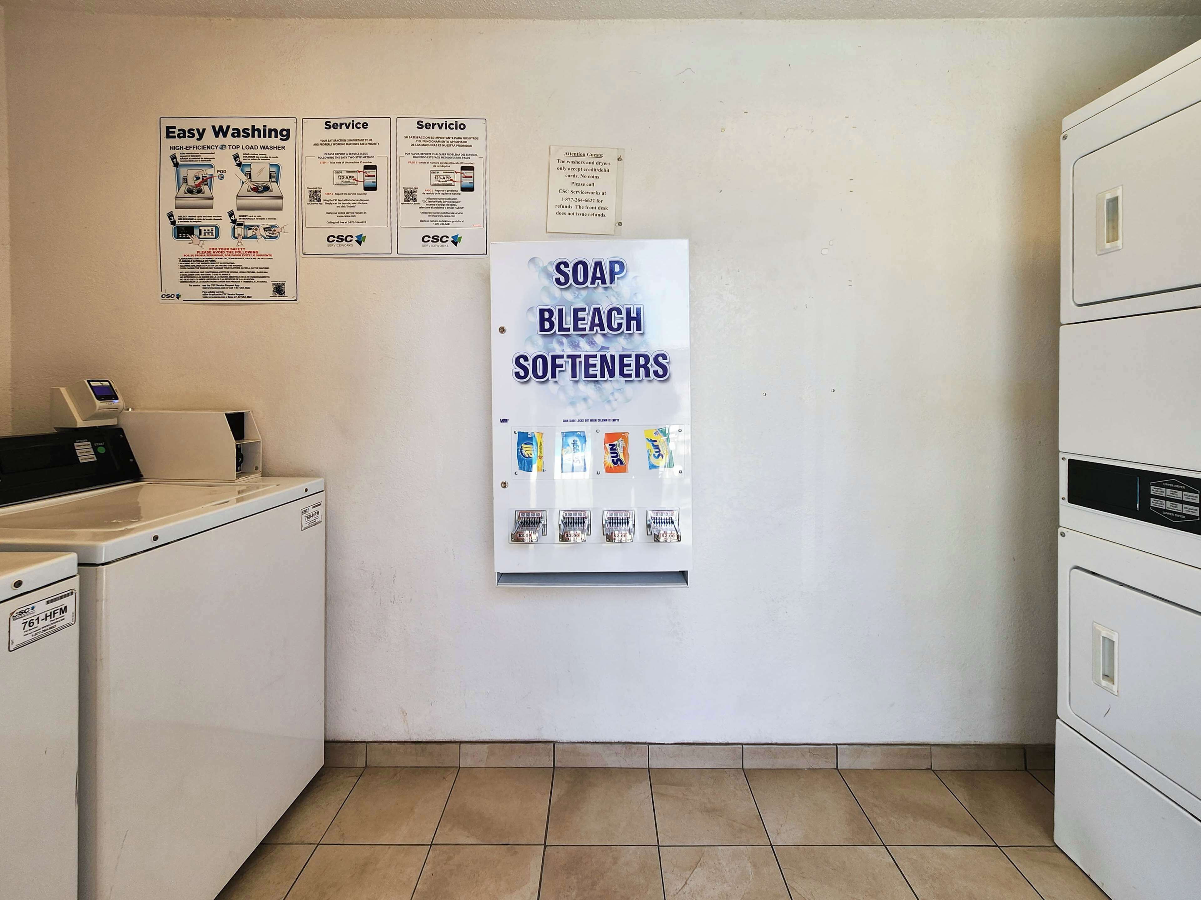 A laundry area with a washing machine, a dryer, and a wall-mounted soap and bleach softener dispenser.