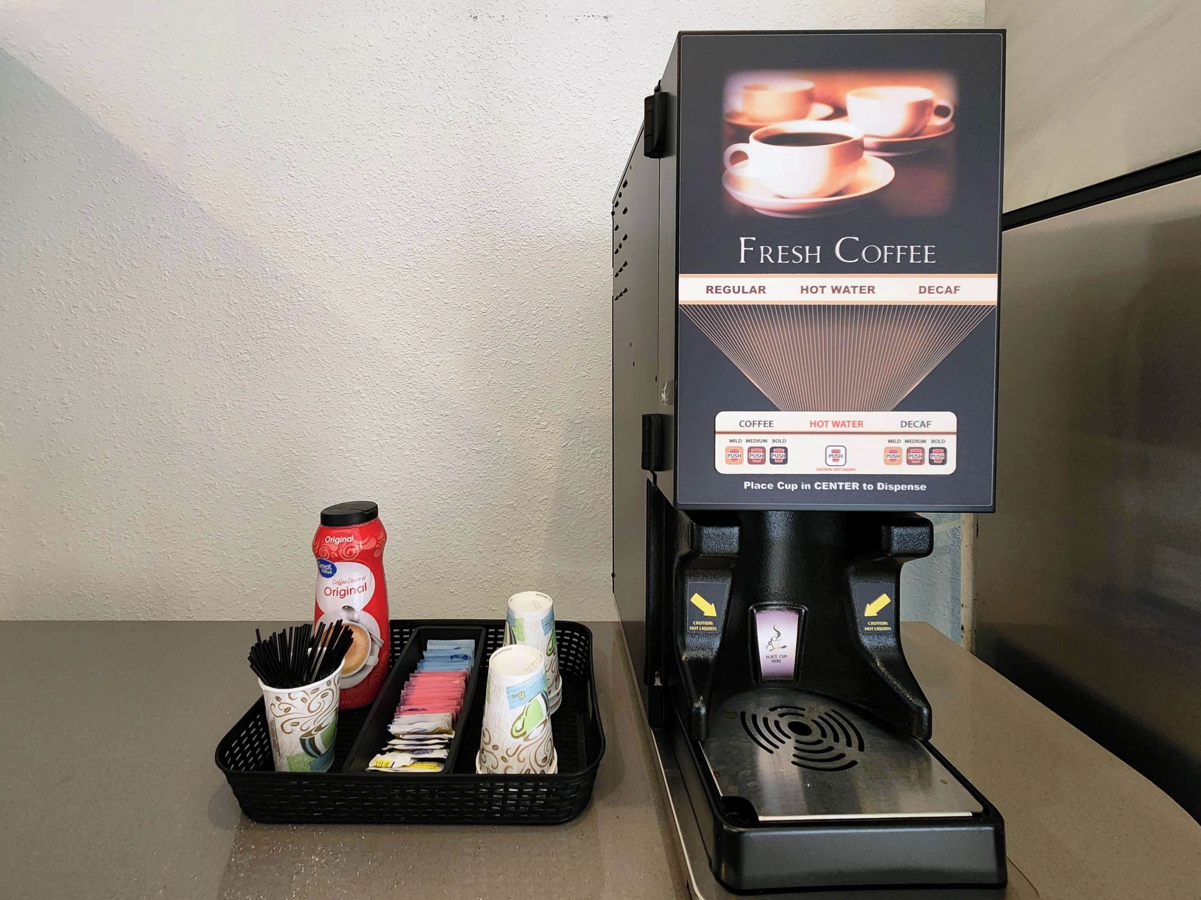A coffee machine with options for regular, hot water, and decaf coffee, along with a cup holder and a basket with coffee cups and utensils.