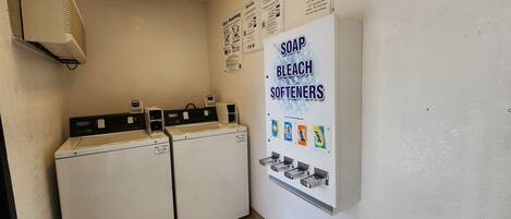 A laundry area with two washing machines and a wall-mounted dispenser for soap, bleach, and softeners.