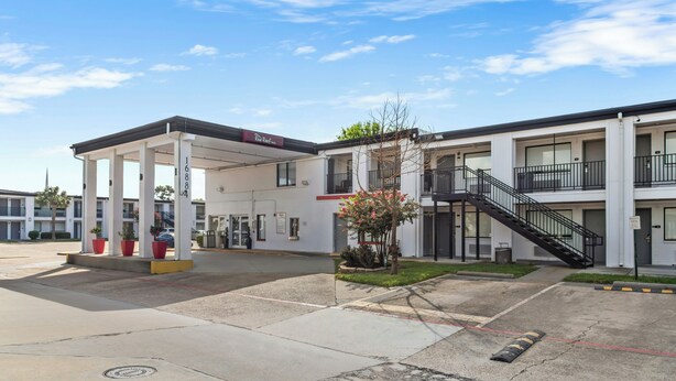 A Red Roof Inn with a covered parking area, a staircase, and a small garden. - Red Roof Inn Houston – Jersey Village (Houston)