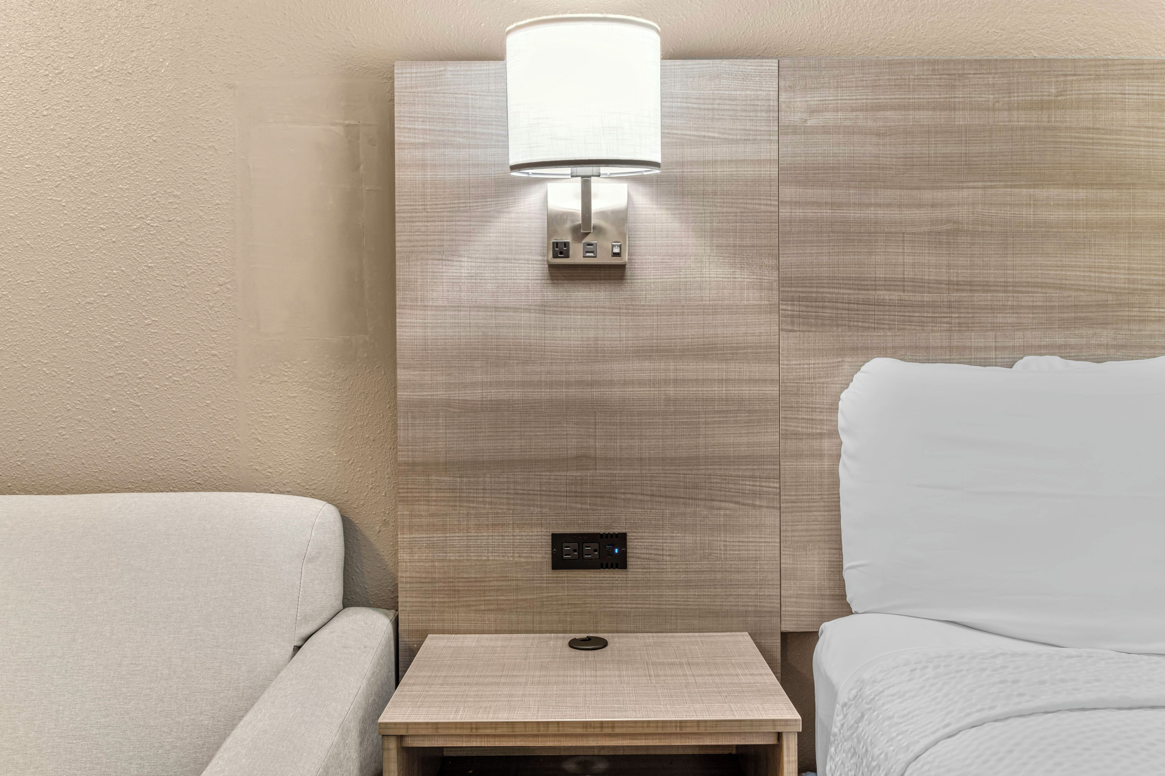 A hotel room with a bed, a nightstand, and a wall-mounted lamp.