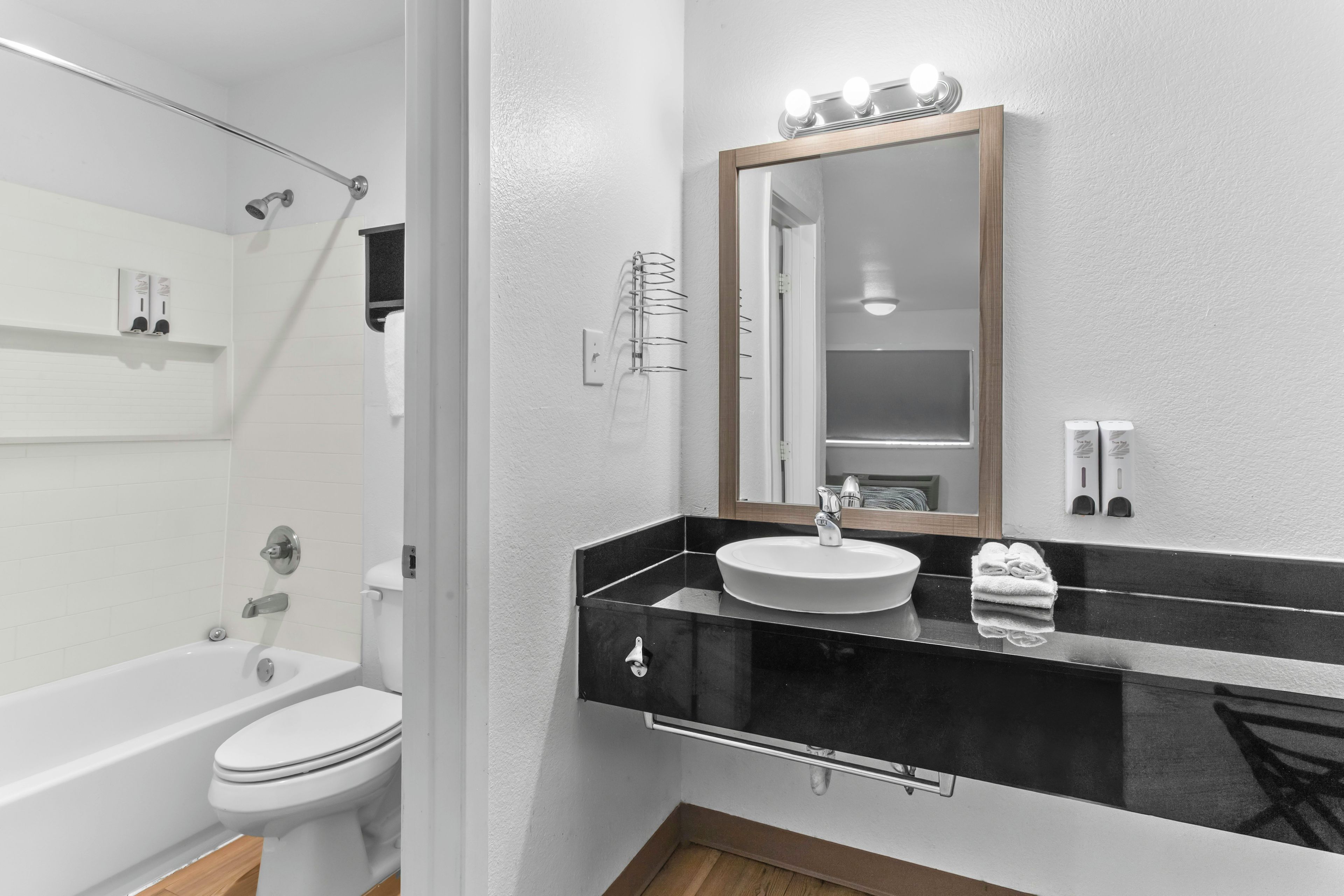 Un baño moderno con inodoro blanco, lavabo negro y espejo con iluminación.