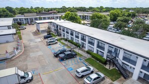 A parking lot with multiple cars and a truck, adjacent to a building with a flat roof and a staircase leading to a second floor. - Red Roof Inn Houston – Jersey Village (Houston)