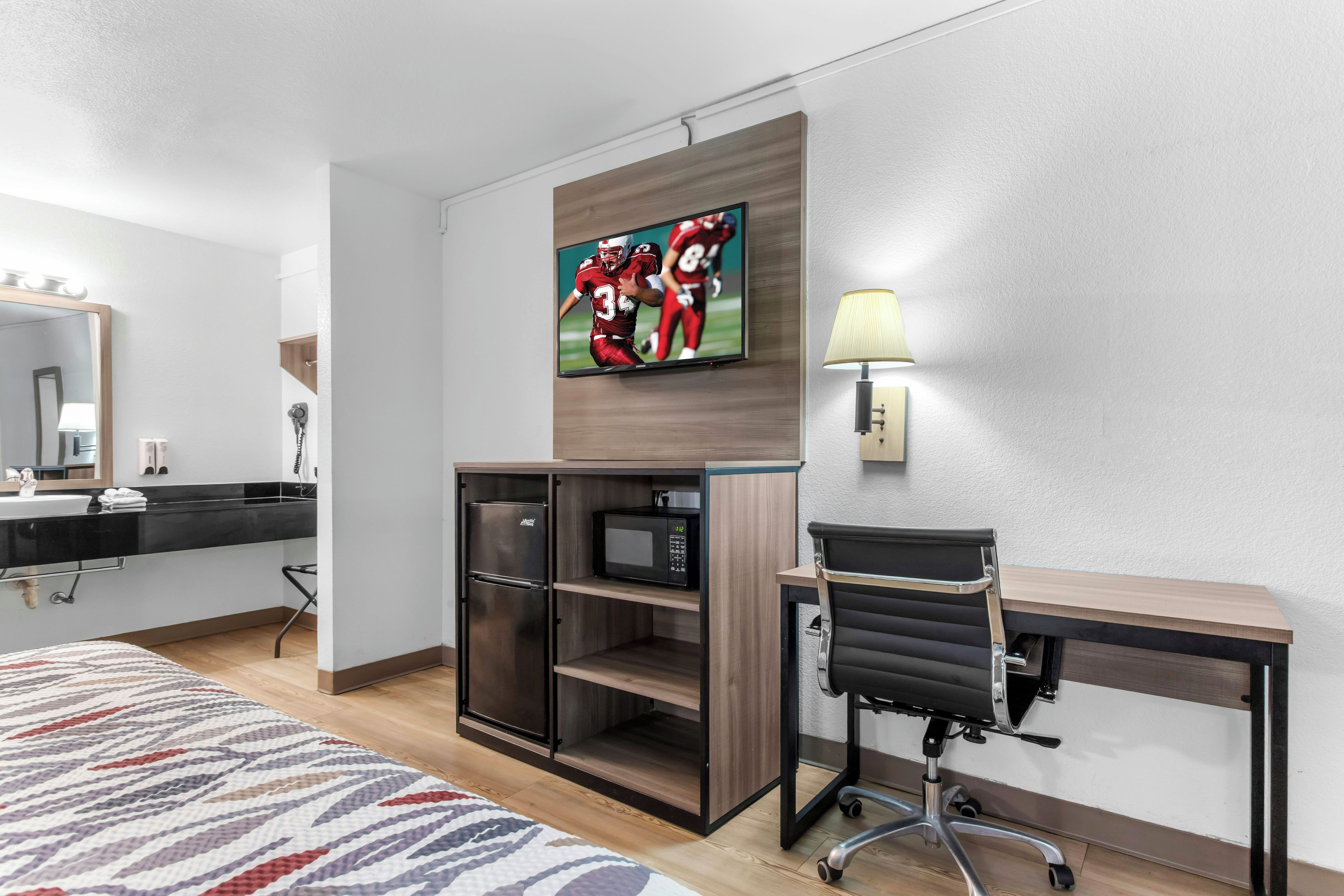 Een hotelkamer met een bed, bureau, stoel, televisie, magnetron en koelkast.