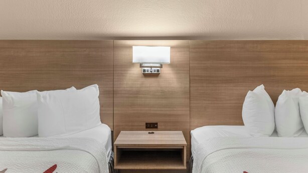 A hotel room with two single beds, a nightstand, a wall-mounted light, and a control panel. - Red Roof Inn Houston – Jersey Village (Houston)