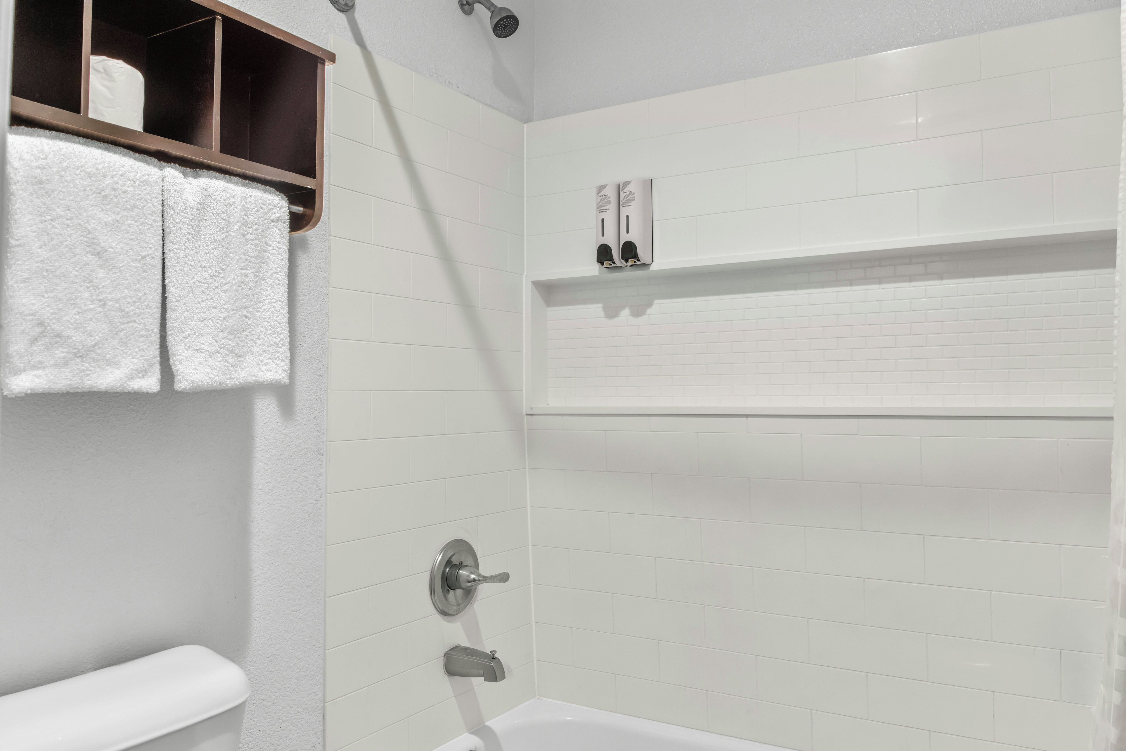 A bathroom with a bathtub, a towel rack with towels, a showerhead, and a soap dispenser.