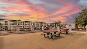 A motel with a parking lot, picnic tables, and a sunset sky. - Red Roof Inn Houston – Jersey Village (Houston)
