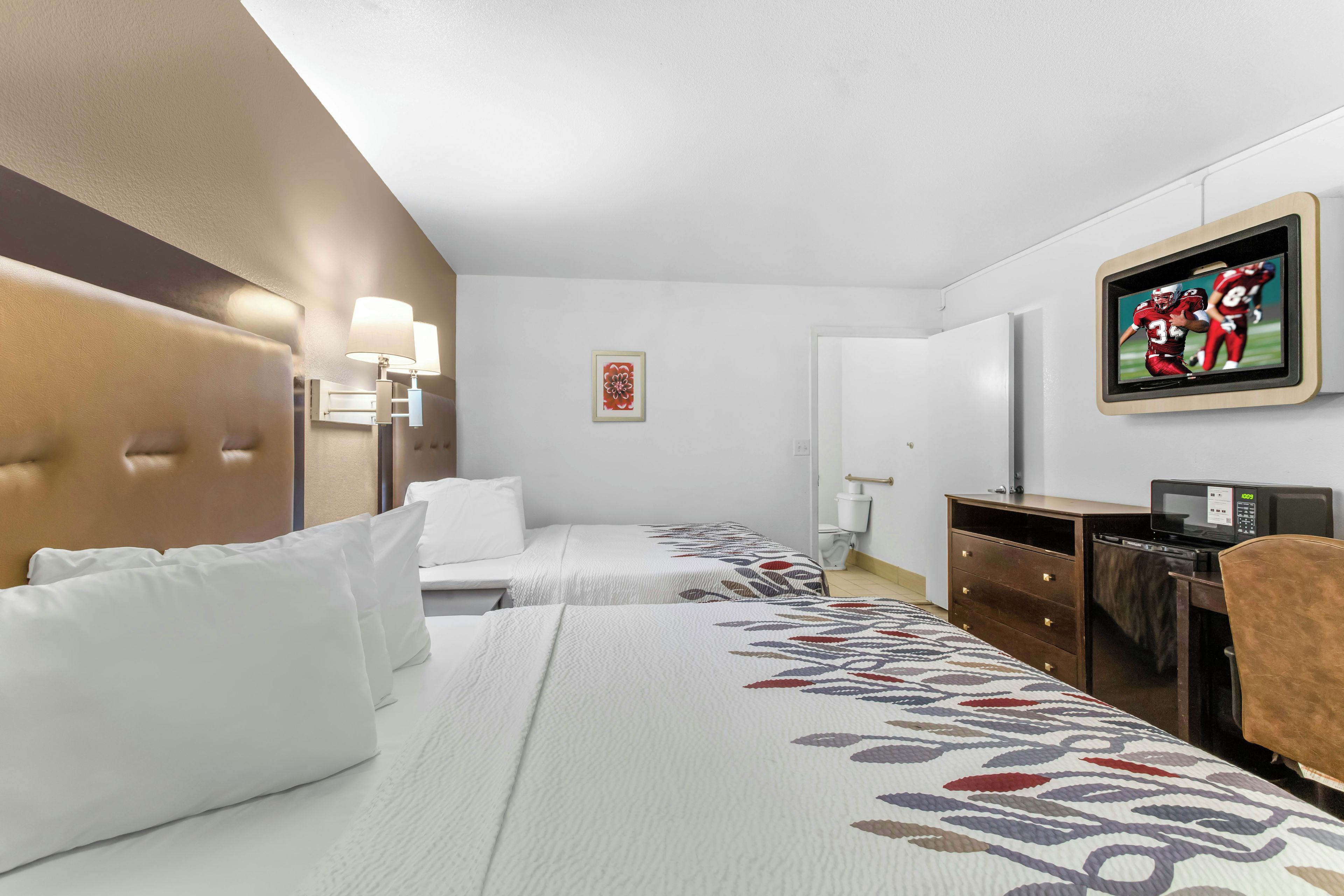 A hotel room with two beds, a television, a desk, and a chair.