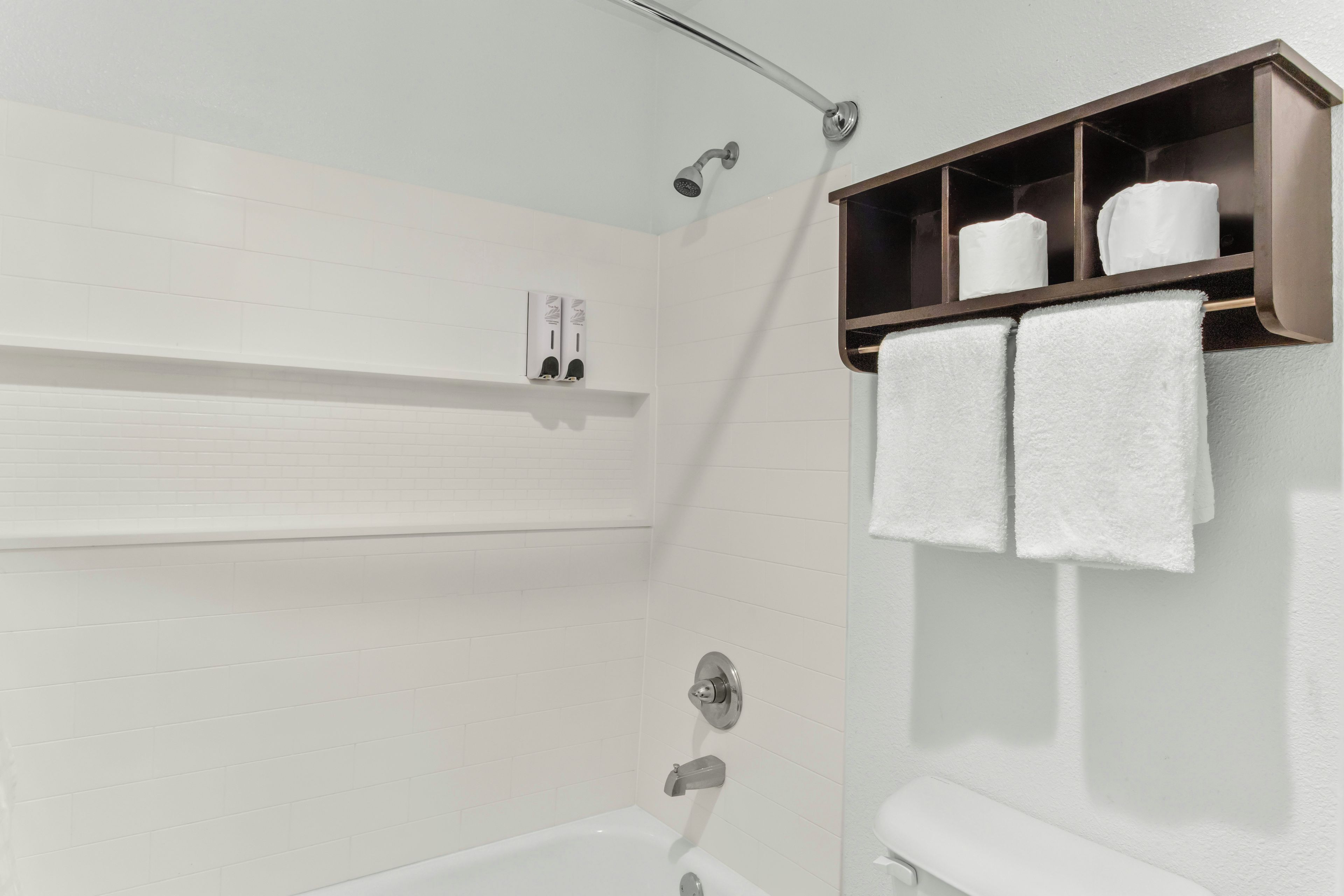Een badkamer met een wit bad, een douche en een handdoekrek met twee handdoeken.