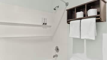 Een badkamer met een wit bad, een douche en een handdoekrek met twee handdoeken.