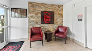 A Red Roof Inn reception area with a stone wall, two leather chairs, a small table, and a doormat. - Red Roof Inn Houston – Jersey Village (Houston)