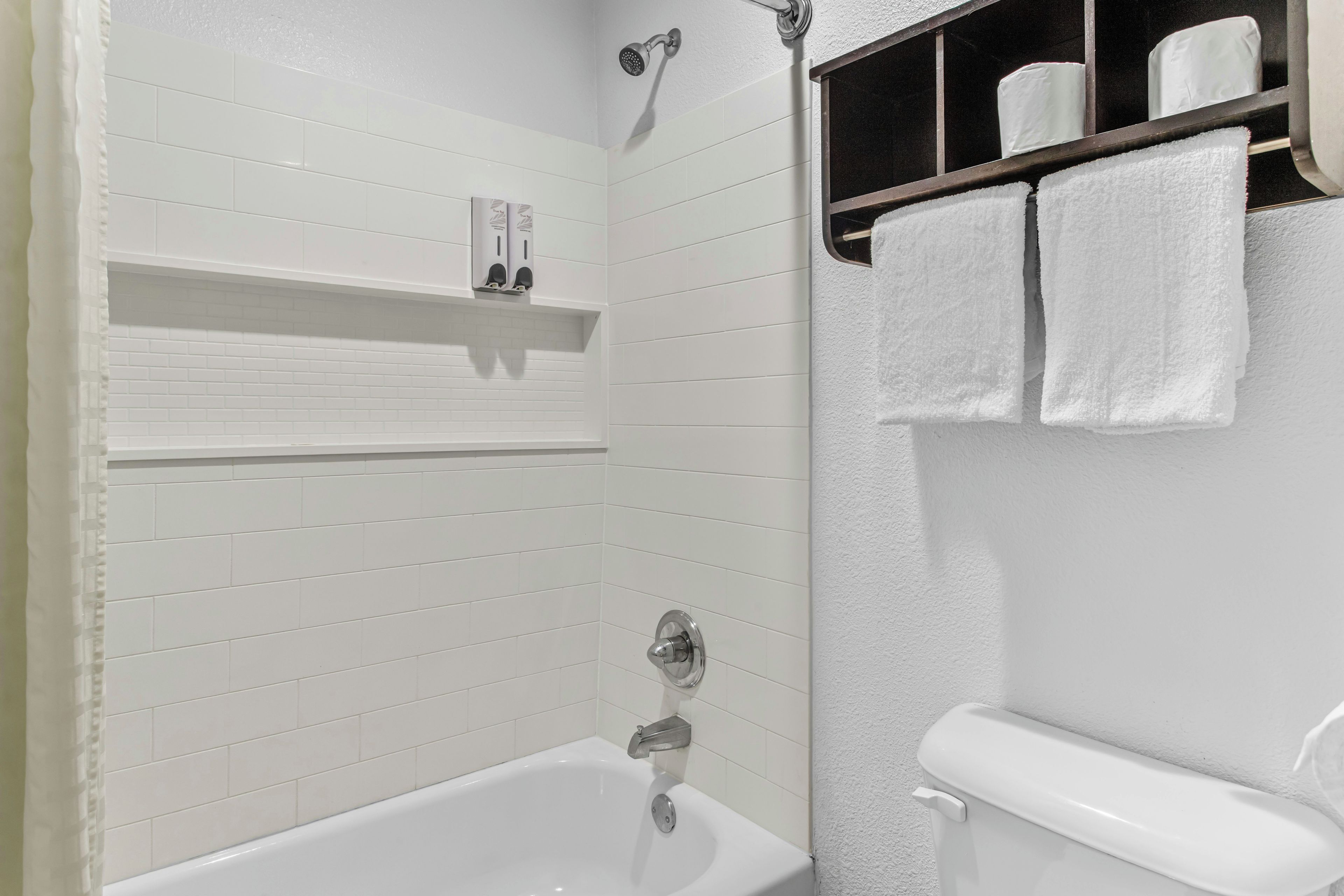 A bathroom with a white bathtub, a showerhead, and a shelf with toiletries.