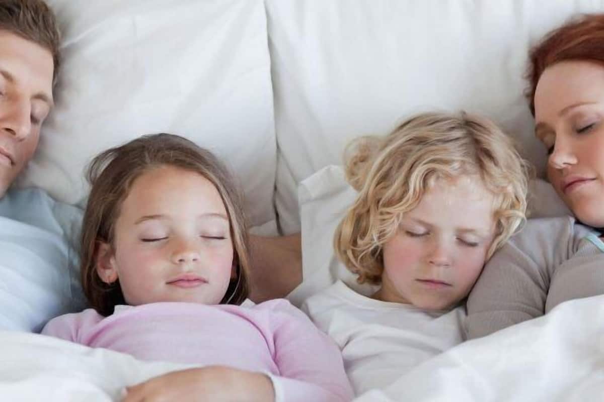 Una familia de cuatro personas durmiendo en una cama con ropa de cama blanca.