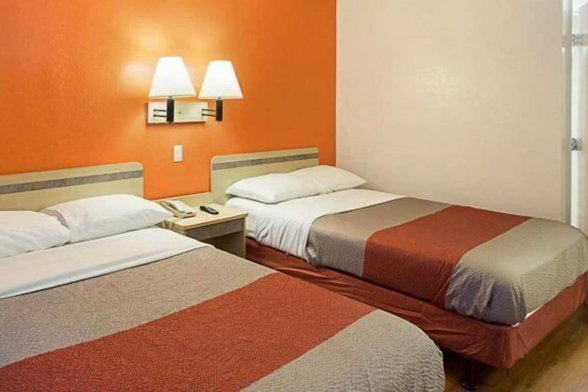 Habitación de hotel con dos camas, una mesita de noche y dos lámparas de pared.