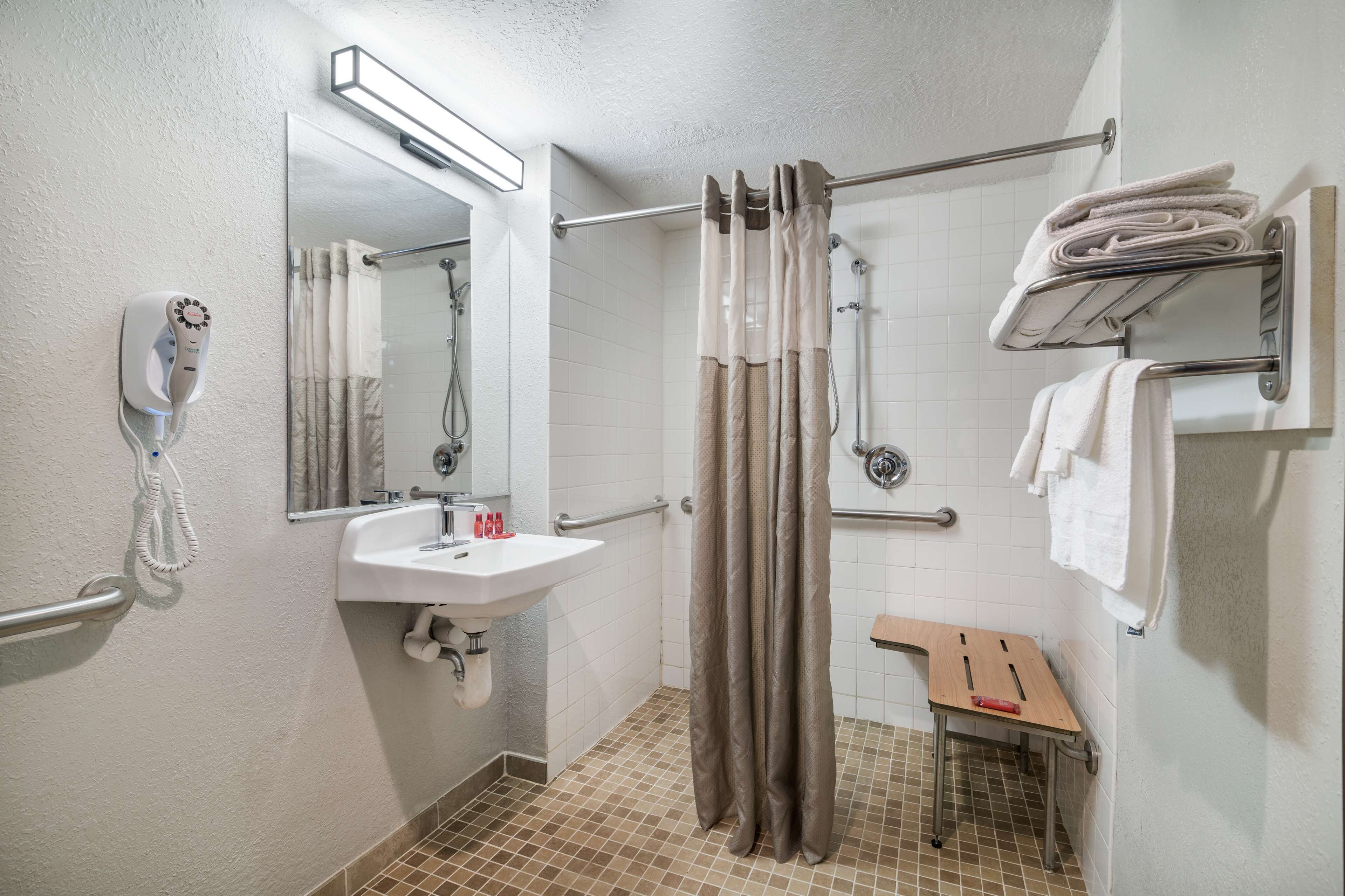 A bathroom with a white sink, a mirror, a shower with a curtain, a towel rack, and a handheld showerhead.
