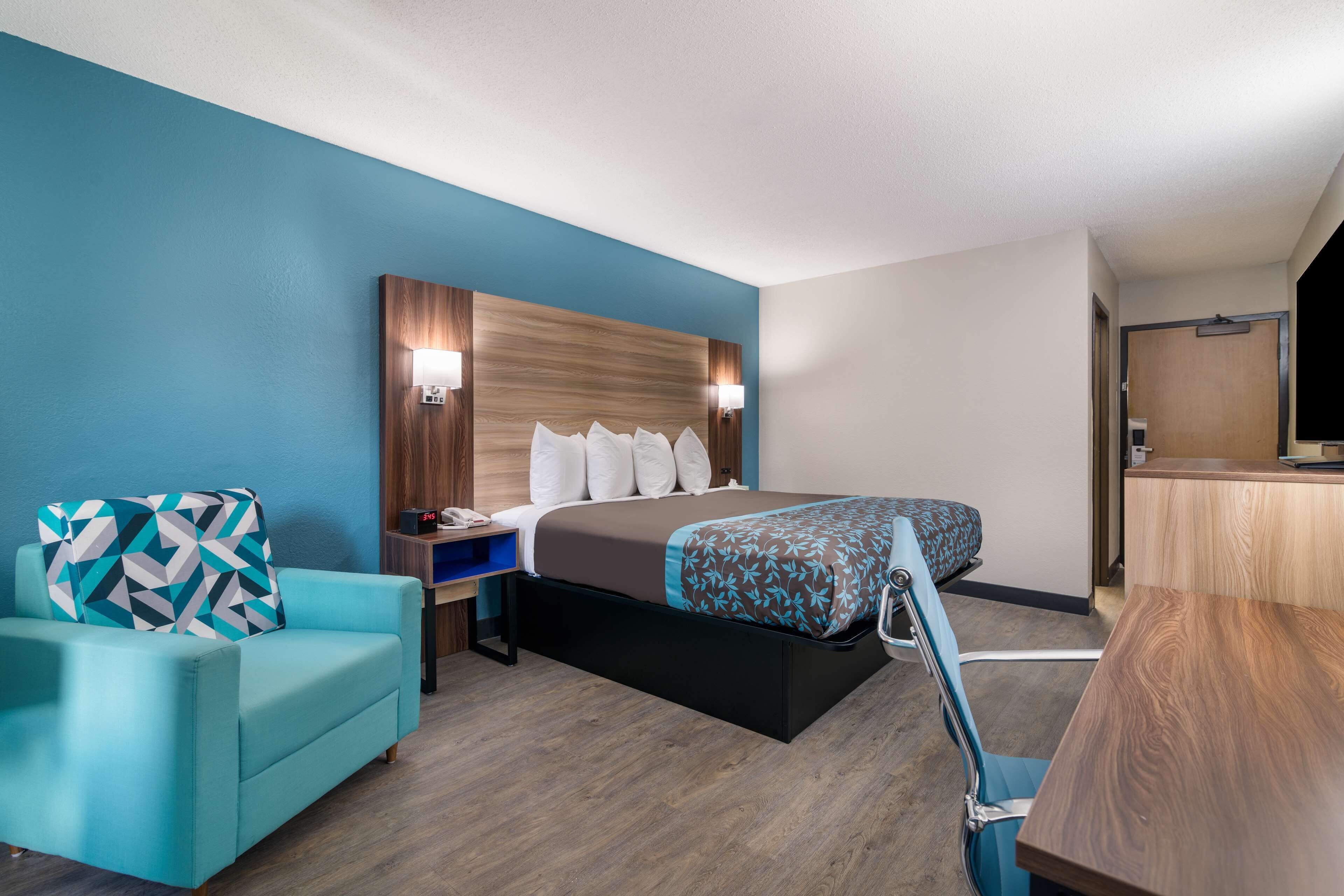 A hotel room with a bed, a desk, a chair, and a TV.