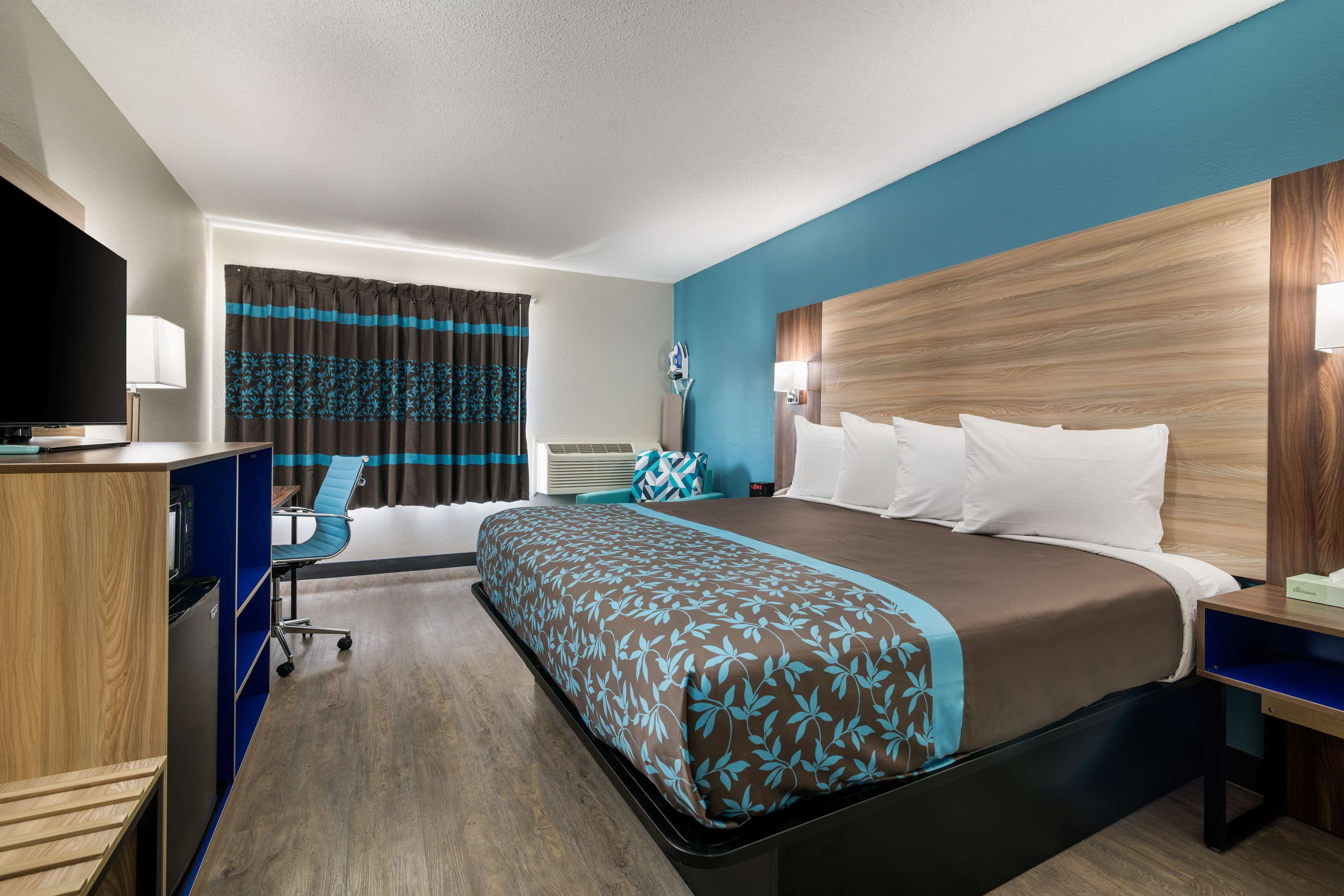 A hotel room with a large bed, a desk with a computer, a chair, a TV, and a window with curtains.