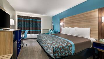 Quarto de hotel com uma cama grande, uma escrivaninha com computador, uma cadeira, uma TV e uma janela com cortinas.