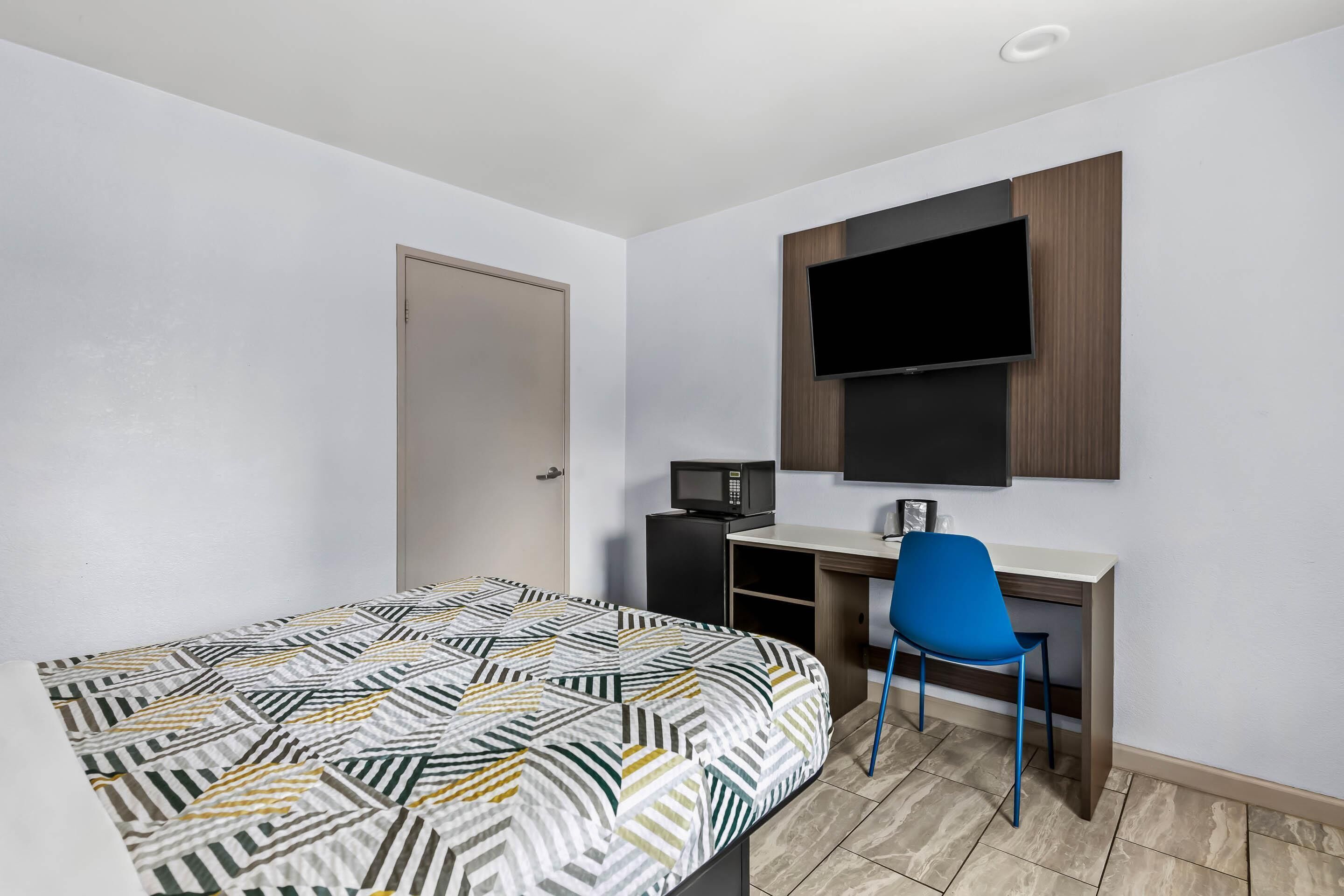 Un dormitorio con cama, escritorio, silla, televisor y microondas.