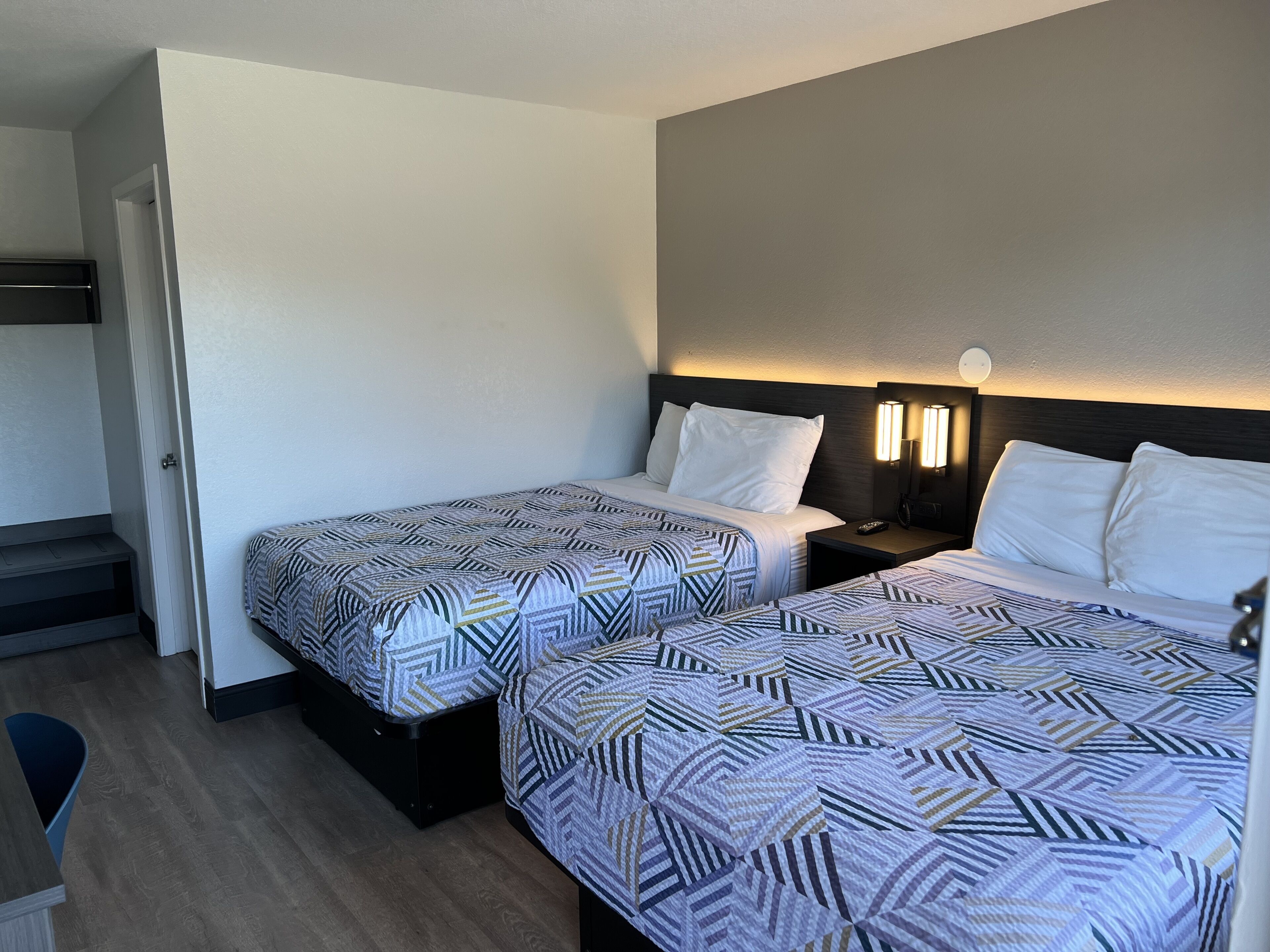 A hotel room with two beds, a nightstand with a lamp, and a staircase.
