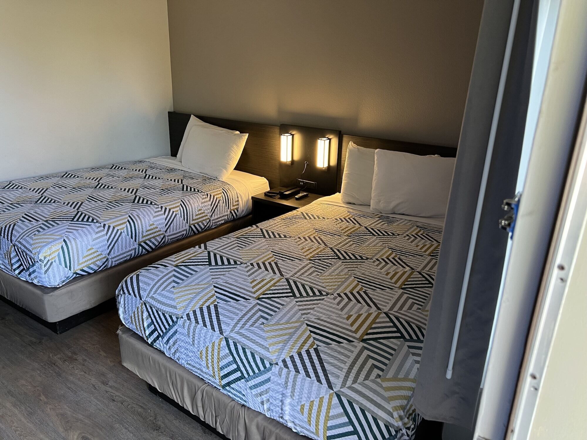 Two single beds with geometric patterned bedding, bedside tables with lamps, and a wooden headboard.