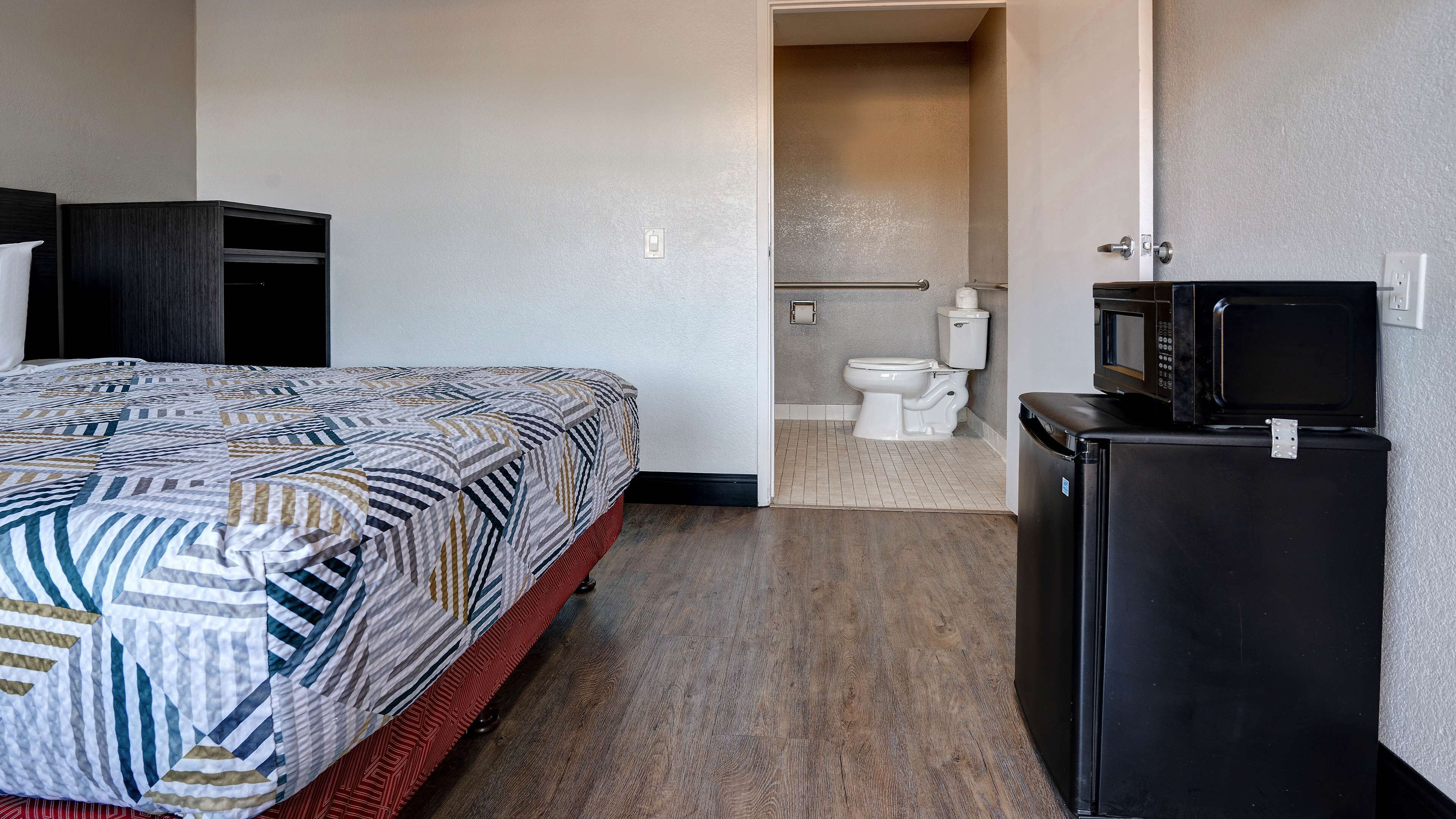 A hotel room with a bed, a small kitchenette, and a bathroom.