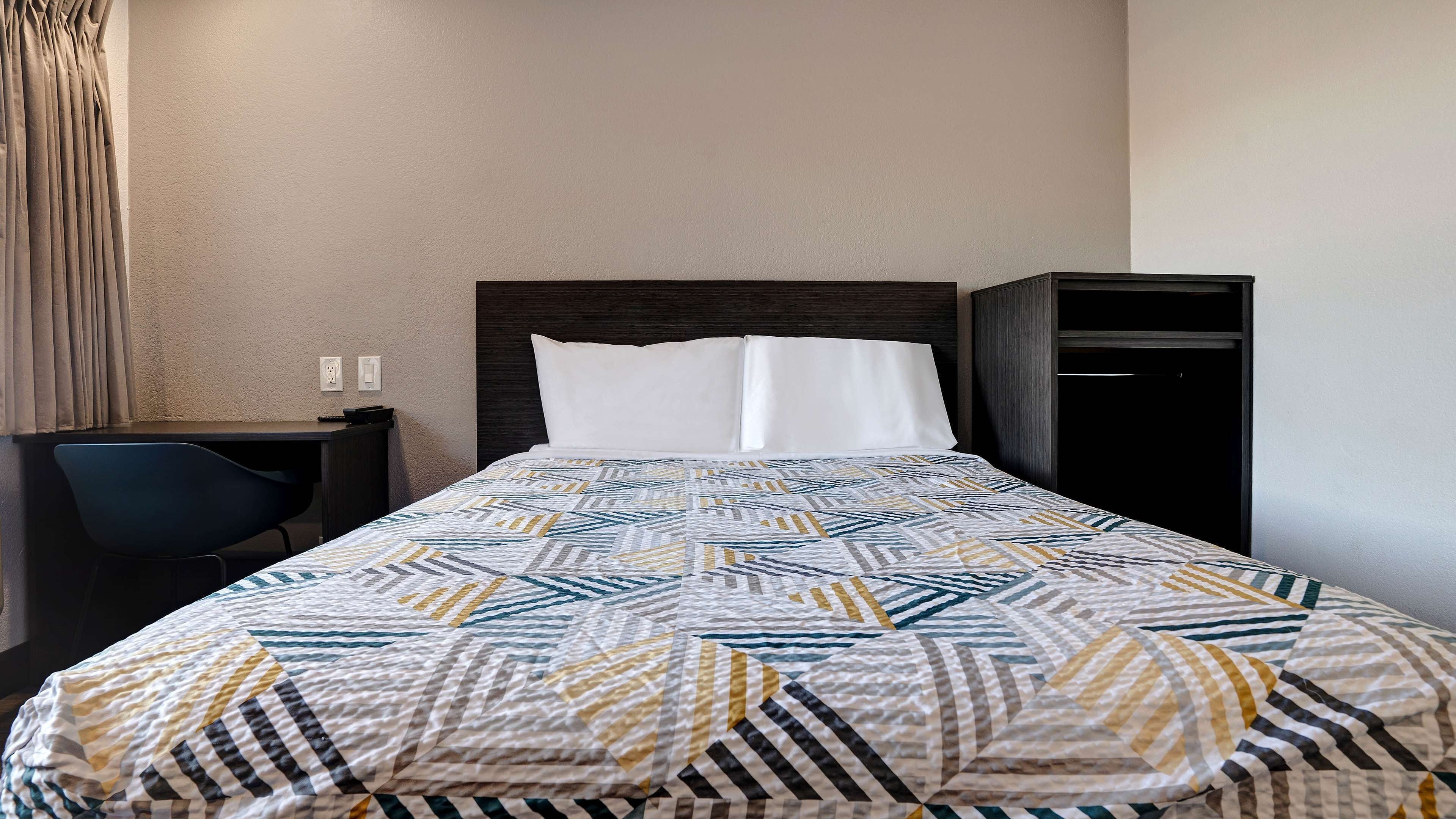 A hotel room with a bed, a desk, and a chair.