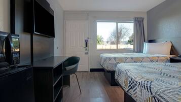 Habitación de hotel con escritorio, dos camas, televisor y ventana con vistas a árboles.