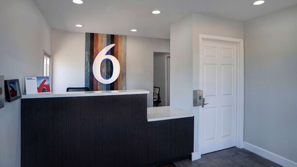 A reception desk with a large number '6' sign, a calendar, and a door with a keypad lock. - Motel 6 Arcata, CA - Cal Poly Humboldt (Arcata)