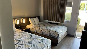 Habitación de hotel con dos camas, una mesita de noche, una lámpara, una ventana con cortinas y vistas al exterior.