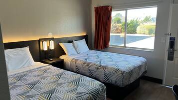 A hotel room with two beds, a nightstand with a lamp, a window with curtains, and a door with a sign.