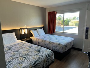 A hotel room with two beds, a nightstand with a lamp, a window with curtains, and a door with a sign. - Motel 6 Arcata, CA - Cal Poly Humboldt (Arcata)