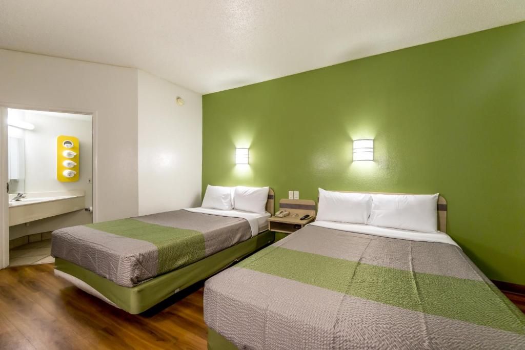 A room with two beds, a bathroom with a mirror, and a green wall.