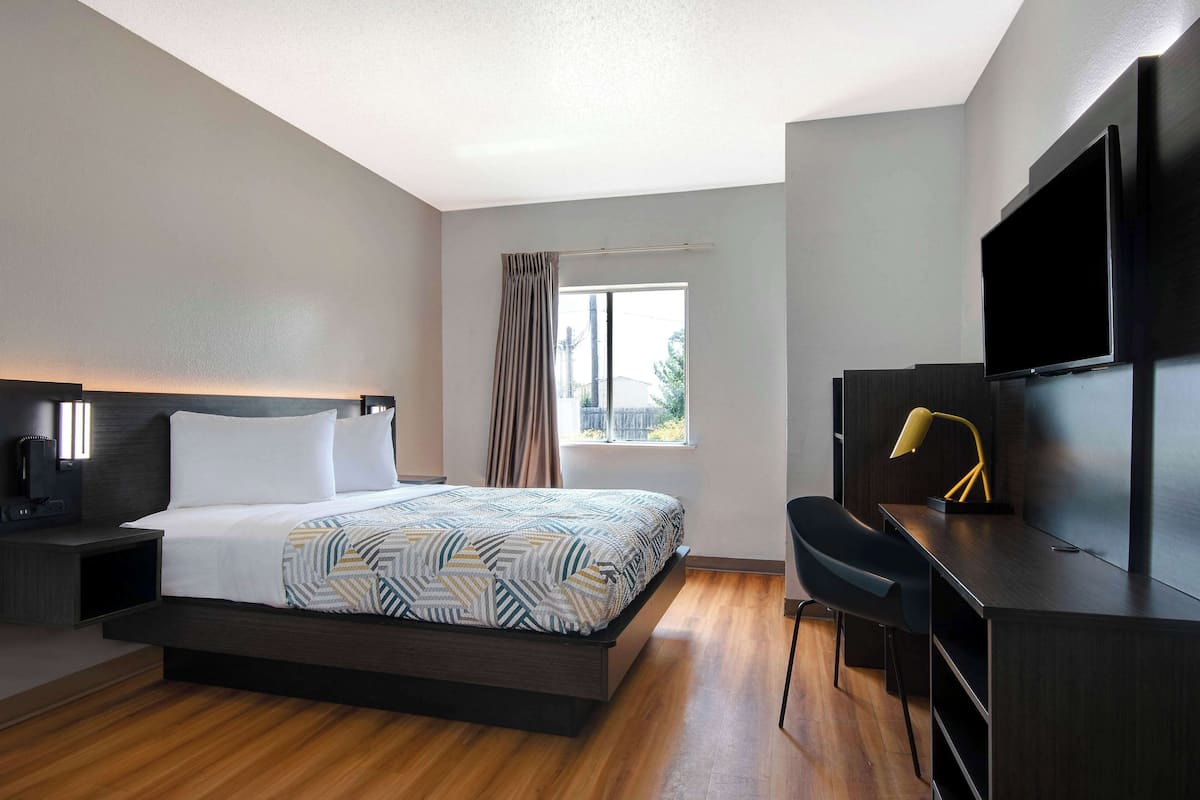 Una habitación de hotel moderna con cama, escritorio, televisor y ventana con cortinas.