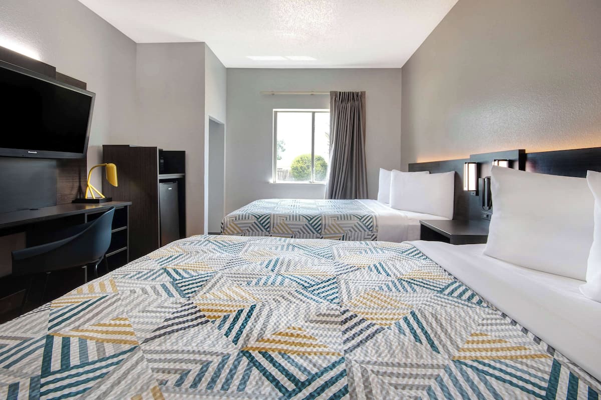 Una habitación de hotel con una cama grande, un escritorio con televisión y una ventana con cortinas.