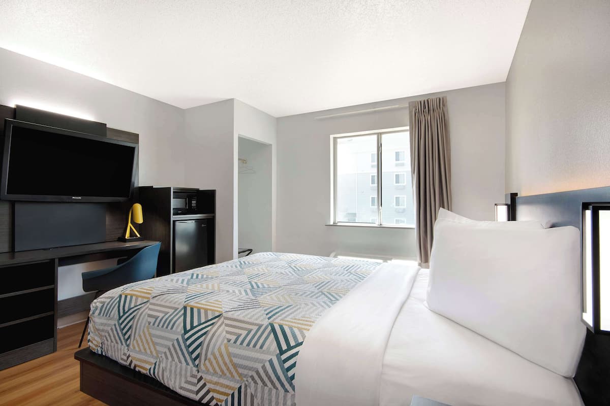 Una habitación de hotel con una cama, un escritorio con televisor, una lámpara y una ventana con cortinas.