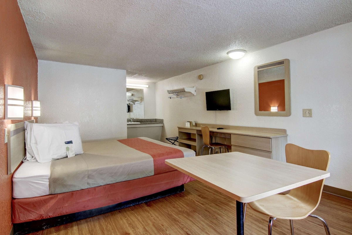 A compact hotel room with a bed, a desk, a chair, a television, and a mirror.