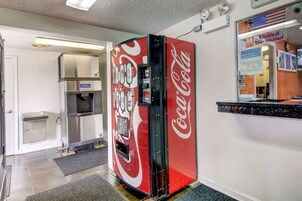 Máquina expendedora de Coca-Cola en el vestíbulo de un hotel, con un microondas y un pequeño cubo de basura.