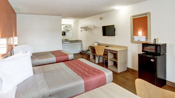 A hotel room with two beds, a desk, a chair, a television, and a microwave.