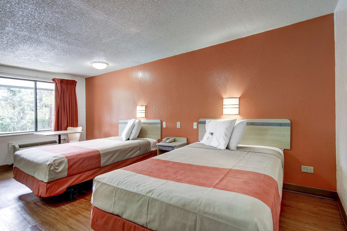 A hotel room with two beds, a desk, a chair, and a window with curtains.