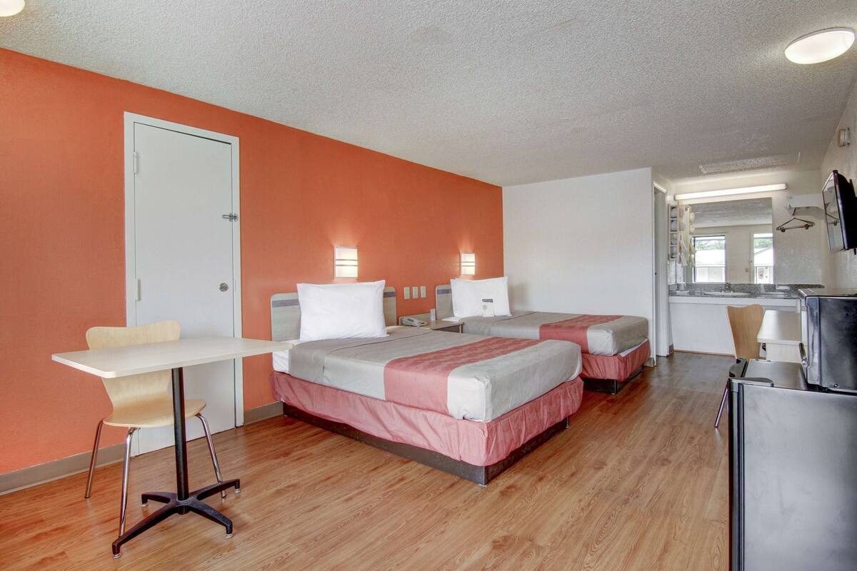 A hotel room with two beds, a desk, a chair, a refrigerator, and a kitchenette.