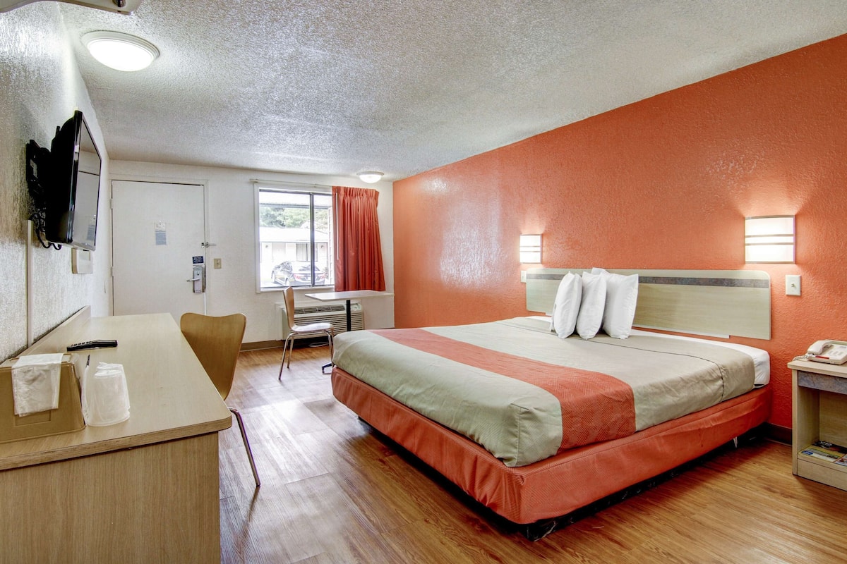 A hotel room with a bed, desk, chair, and a window with curtains.