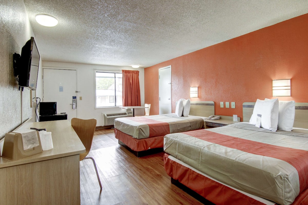 A hotel room with two beds, a desk, a chair, a TV, and a window with curtains.